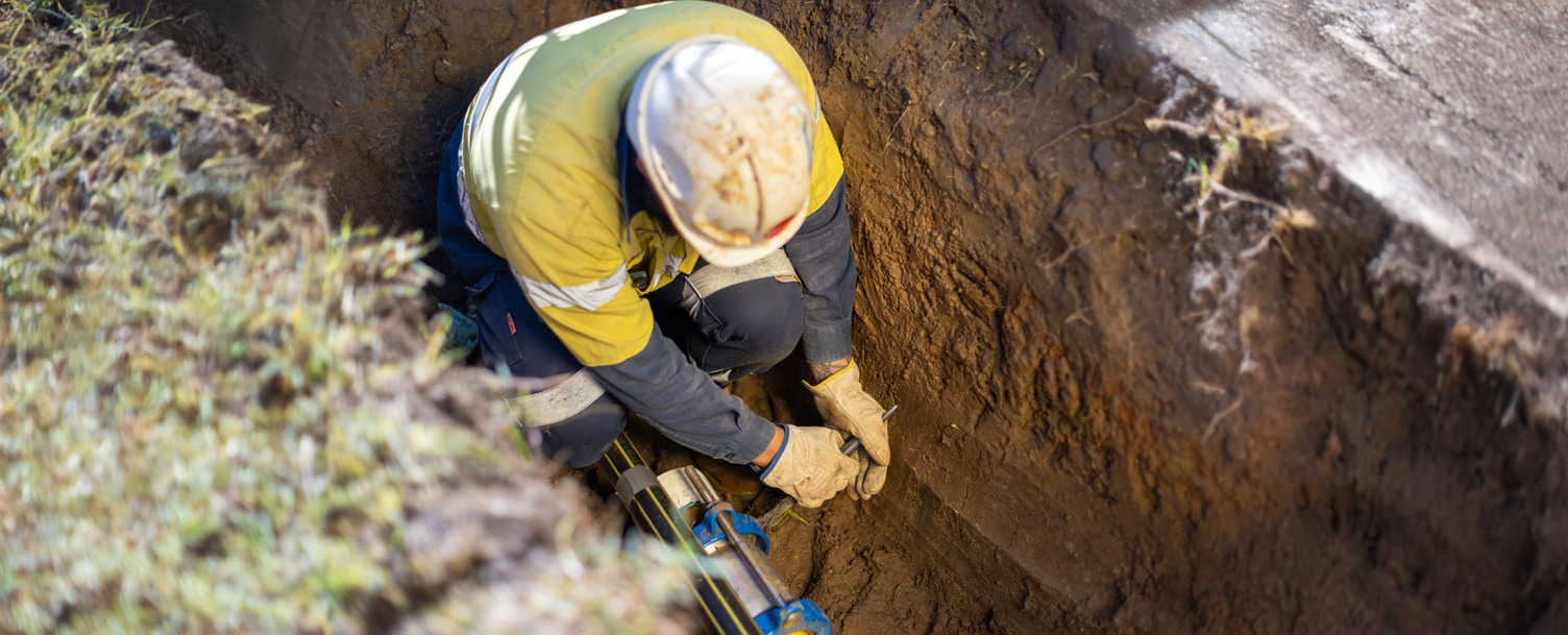A worker wearing high vis working on a gas pipe in a trench