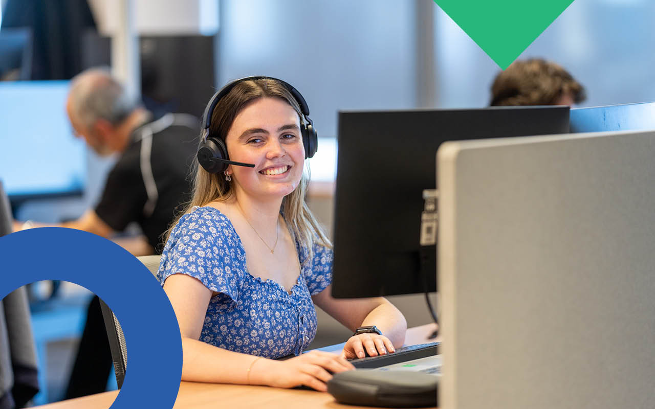 A smiling woman wearing a headset at a desk