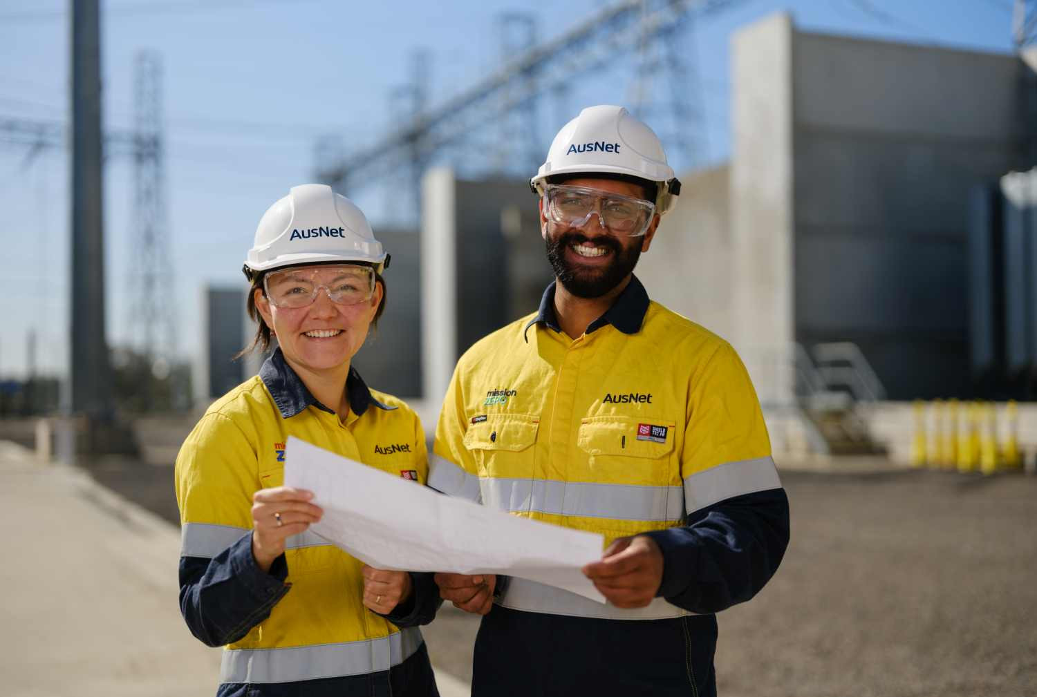 Two smiling workers outside, wearing high vis and holding a document together