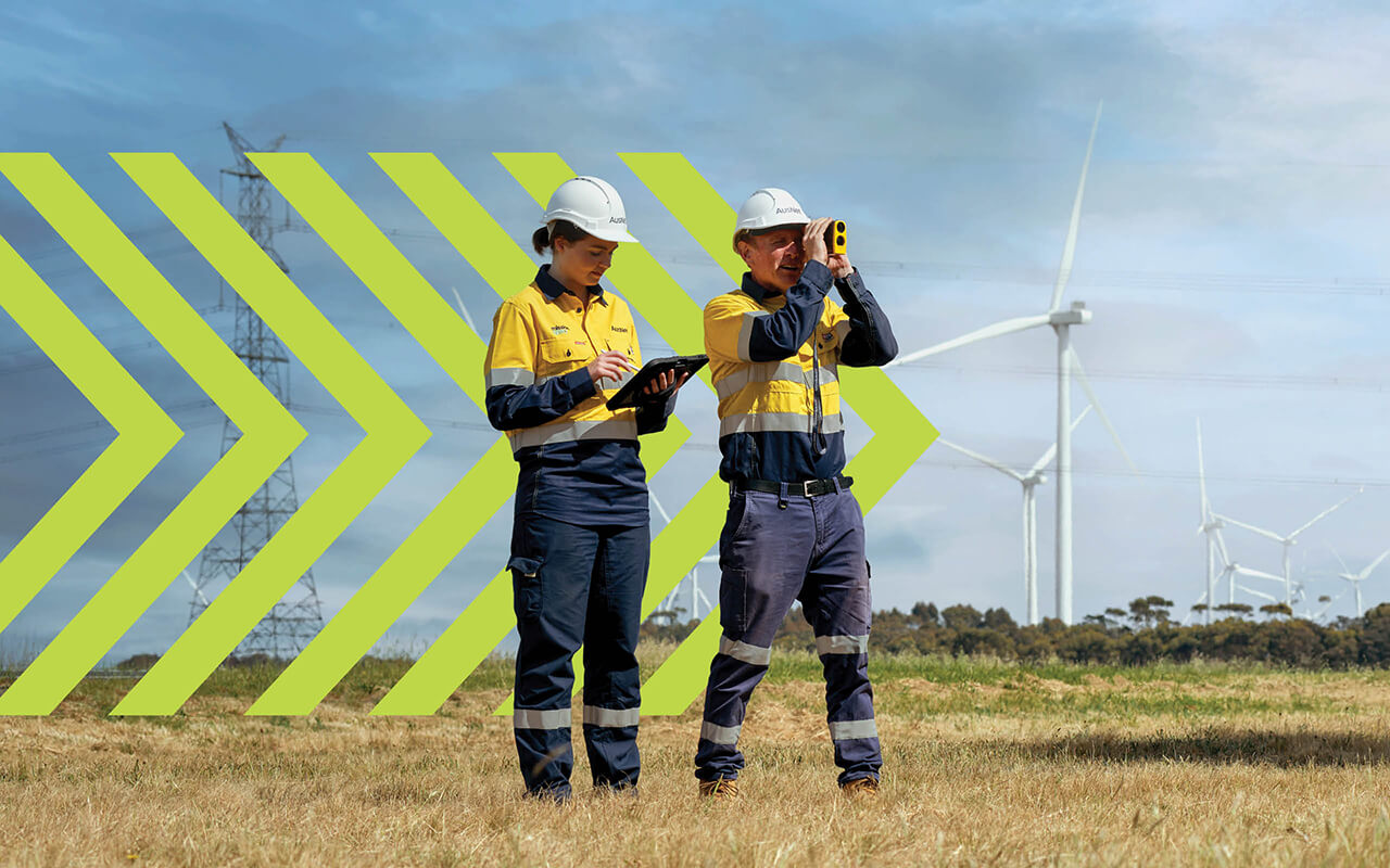 Two high vis workers in an field, one using equipment to view long distance
