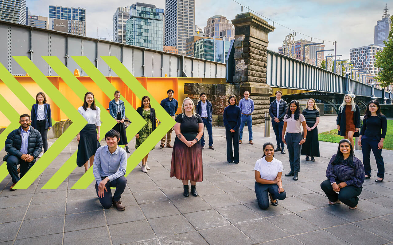 A large group of graduates outside near a bridge, posing for a photo