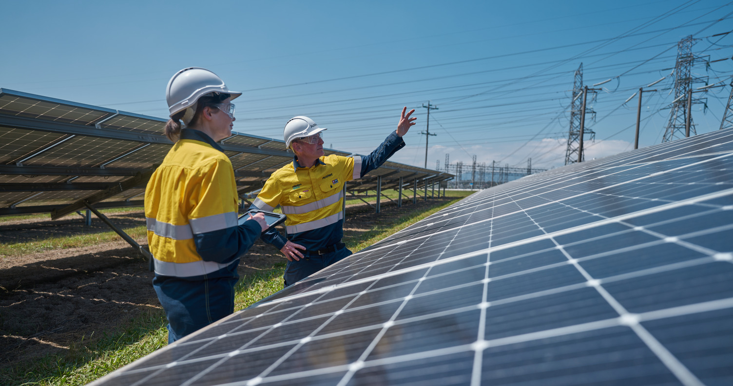 Two workers outside near a large solar panel